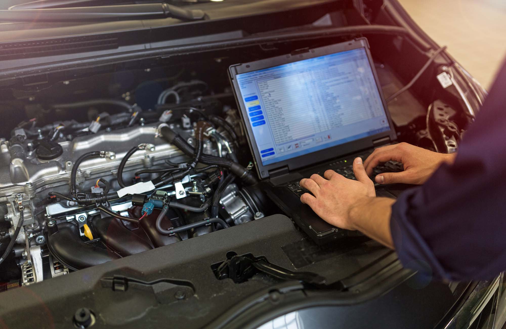 Mechanic Using Laptop While Examining Car Engine. Hands of mechanic working on car engine in auto repair shop